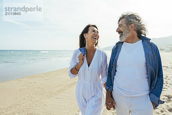 Happy senior woman holding hands with man and walking at beach