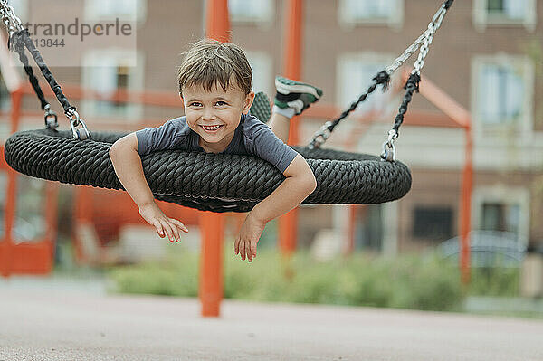 Cheerful boy swinging on swing at park