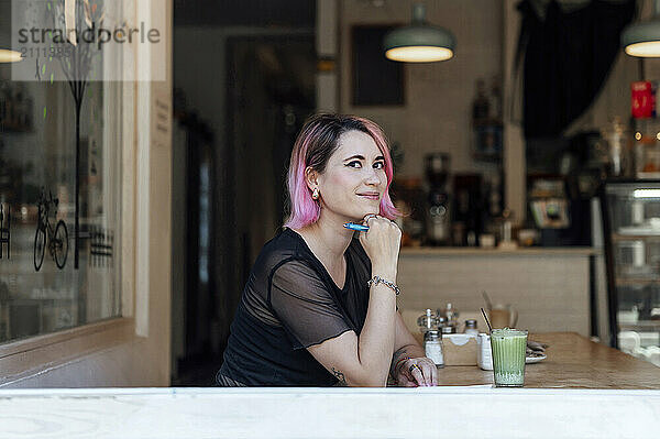 Smiling hipster woman leaning on elbow and sitting in cafe