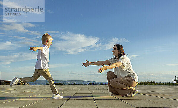 A happy boy in a white shirt runs to his mother.