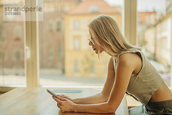 Focused blond woman sitting and using smart phone in cafe