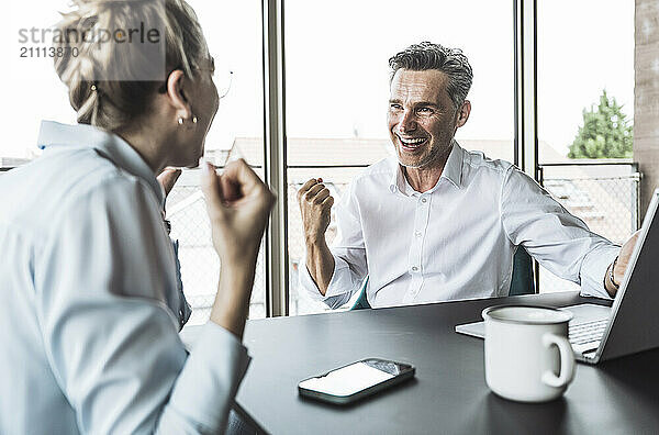 Happy successful businessman and businesswoman sitting at desk