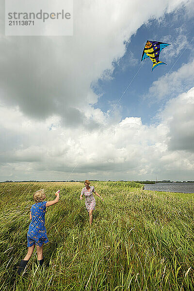 Mother and daughter flying kite in agricultural field