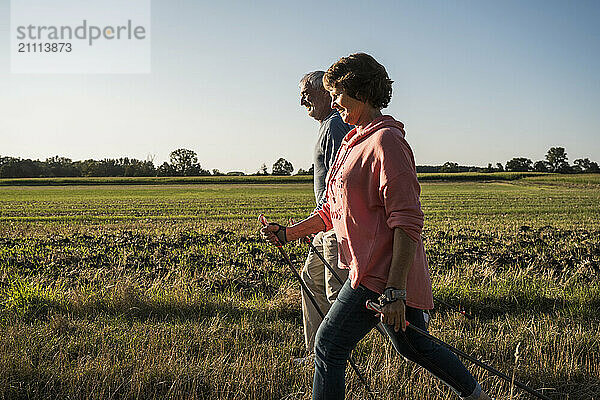 Senior couple with hiking poles walking near field