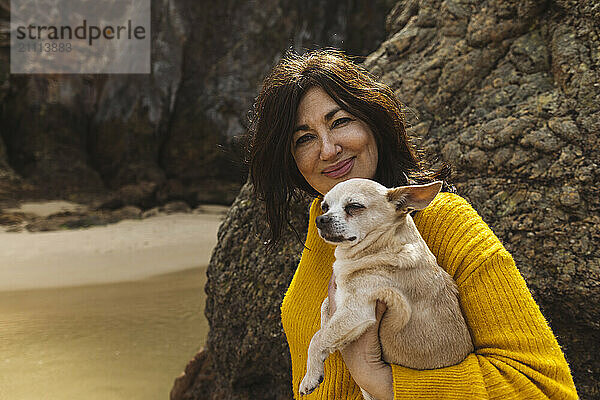 Senior woman carrying dog near mountain at beach