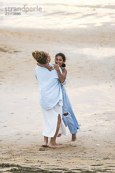 Playful woman picking up granddaughter at beach