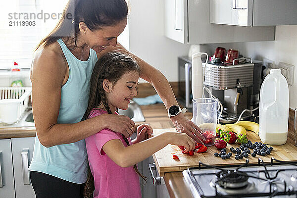 Happy mother and daughter preparing milkshake in kitchen at home