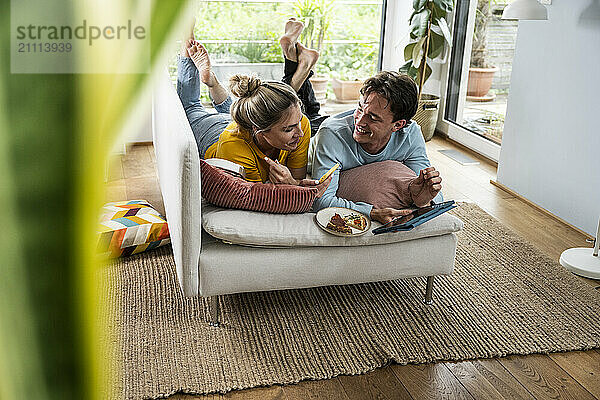 Smiling young couple spending leisure time lying on sofa at home