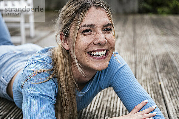 Cheerful blond woman spending leisure time lying on wooden patio