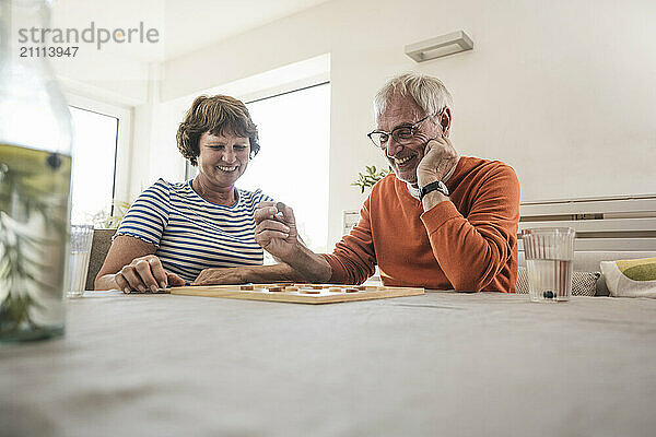 Senior man with hand on chin playing board game with wife at home