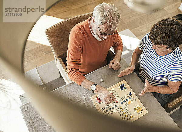 Senior couple sitting near table and enjoying ludo at home