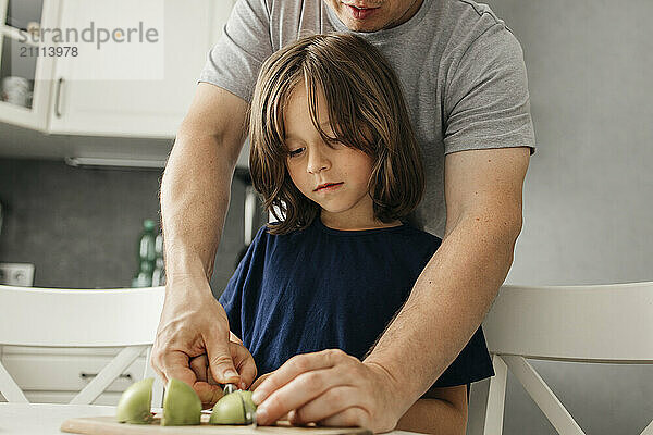 Son with father cutting apple in kitchen