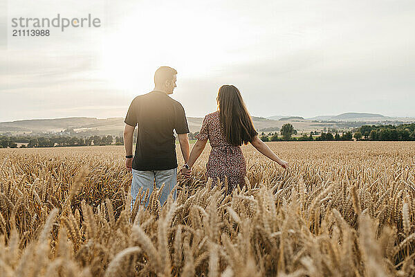 Couple holding hands and standing in agricultural field at sunset