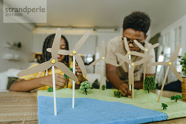 Brother and sister making wind turbines project at table in living room