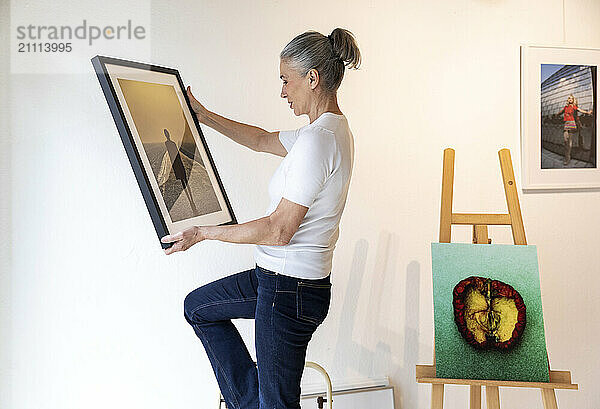 Painter holding picture frame and standing near wall in studio