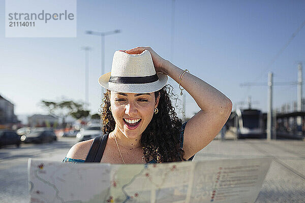 Happy woman wearing hat looking at map on sunny day