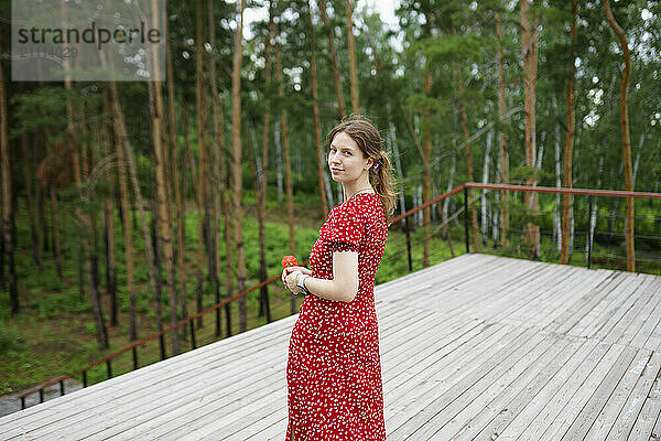 Woman holding flower and standing on patio near forest