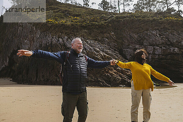 Senior couple standing with arms outstretched at beach