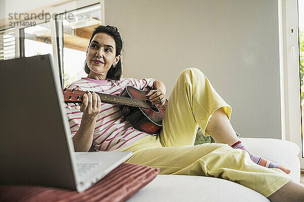 Woman playing guitar sitting on sofa at home