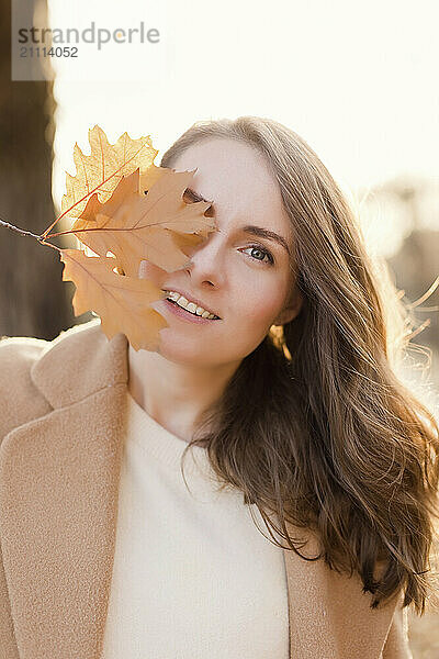 Beautiful woman covering eye with maple leaf