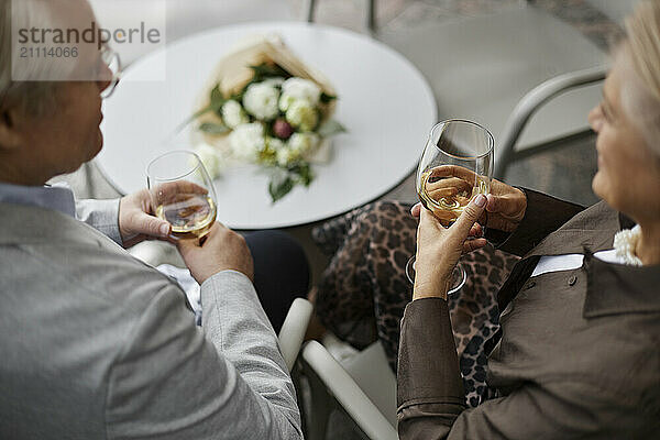 Senior couple holding wine glass and sitting near table at outdoor restaurant