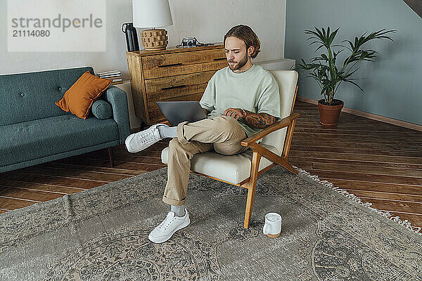 Freelancer using laptop sitting on armchair at home