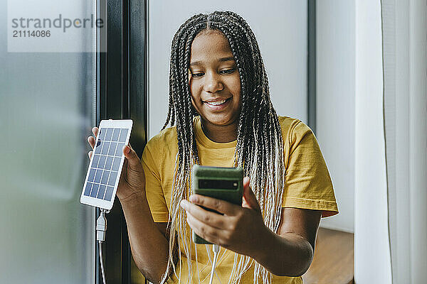 Happy girl charging mobile phone with solar panel equipment at home