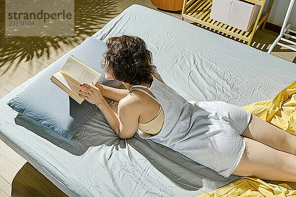 Relaxed woman reading book on bed at home