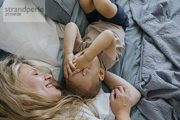 Playful mother and son lying on bed at home