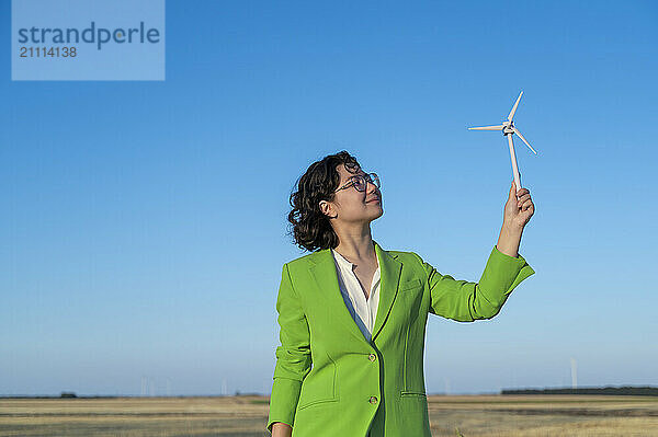 Engineer in green blazer holding wind turbine model at farm