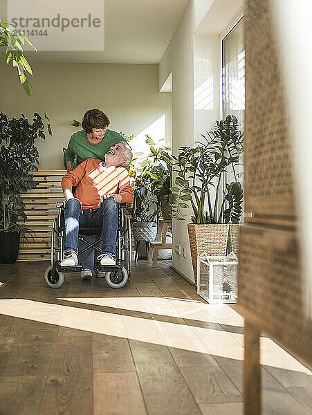 Senior woman assisting husband on wheelchair at home