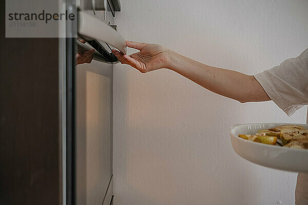 Woman's hand putting pears in oven at home