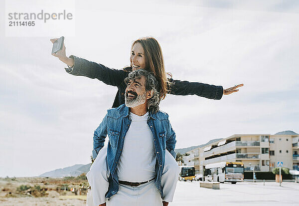 Happy senior man piggybacking woman and taking selfie