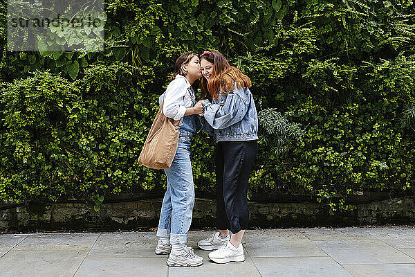 Young woman kissing girlfriend standing on sidewalk at park