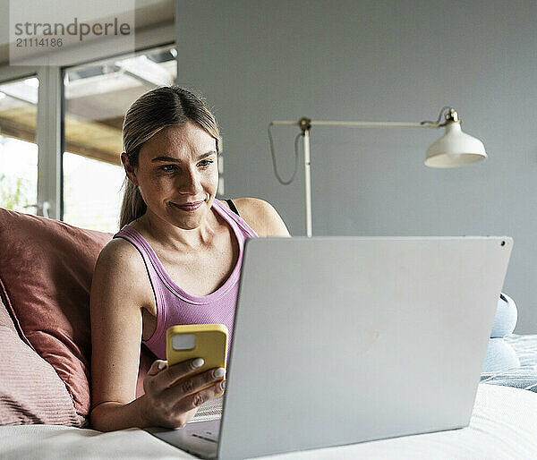 Smiling young woman using wireless technologies on sofa at home