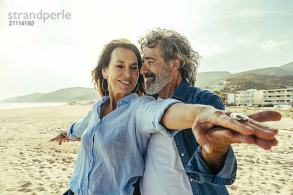 Happy man and woman standing with arms outstretched on sunny day at beach