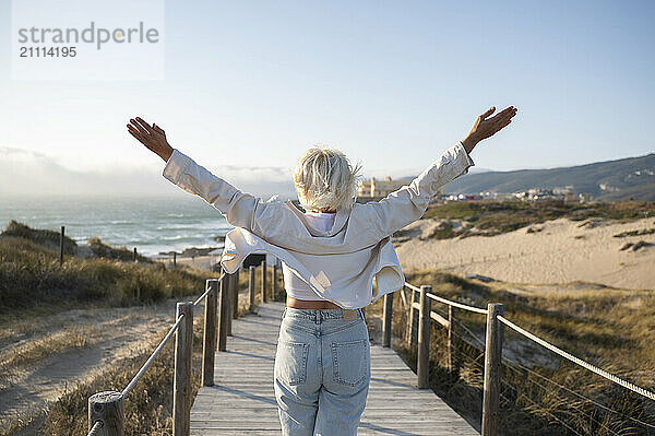 Carefree woman with arms outstretched walking on pier towards sea