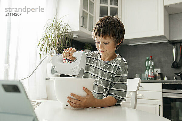 Boy using electric mixer in kitchen