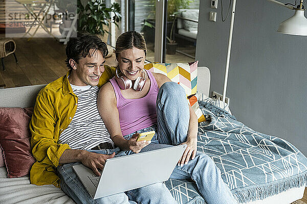 Happy couple using wireless technologies sitting on sofa at home