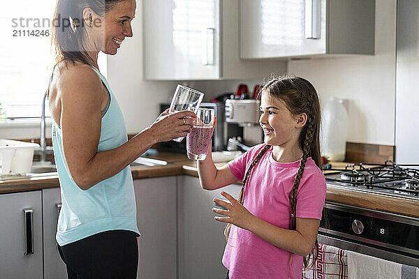 Mother and daughter toasting milkshake glasses in kitchen at home