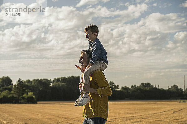 Boy sitting on shoulders of grandfather under cloudy sky