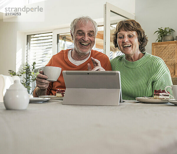 Happy couple sitting near table and using digital tablet for video call at home