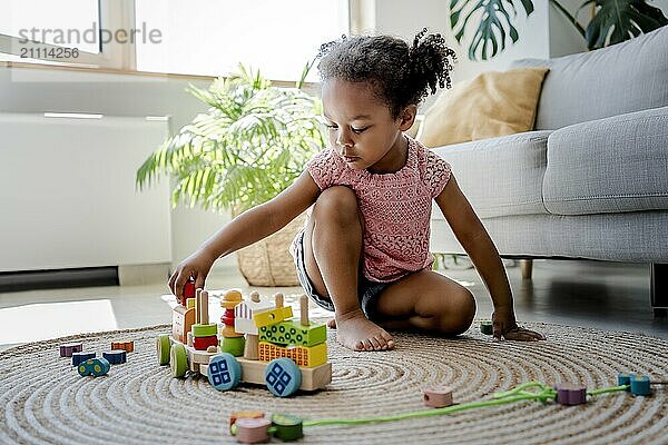 Girl sitting on rug and playing with toy vehicle at home