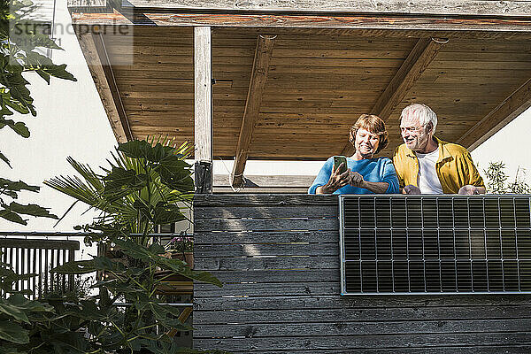 Senior couple using smart phone near solar panel at balcony