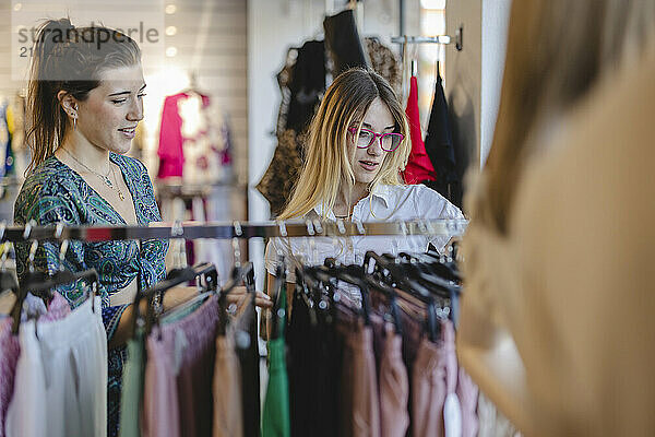 Young friends choosing clothes from rack at modern fashion store