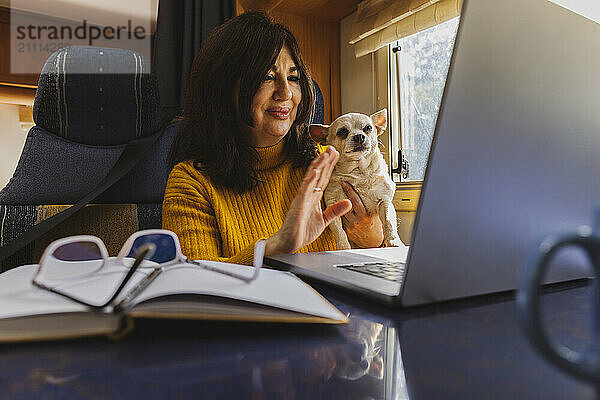 Senior woman attending video call through laptop with dog in motor home