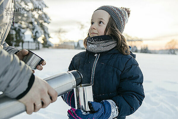 Son holding mug and standing near father in winter