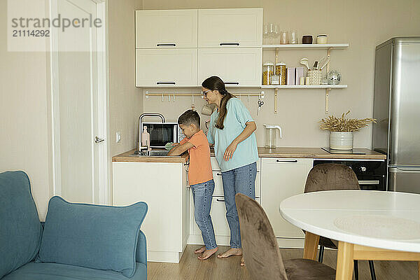 Son helping mother in cleaning kitchen at home