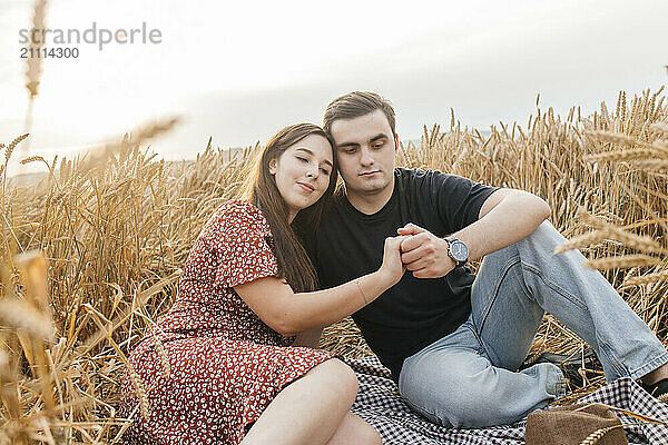 Romantic young couple sitting and holding hand amidst agricultural field