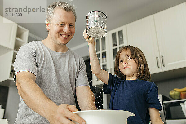 Smiling father with son sifting flour in kitchen